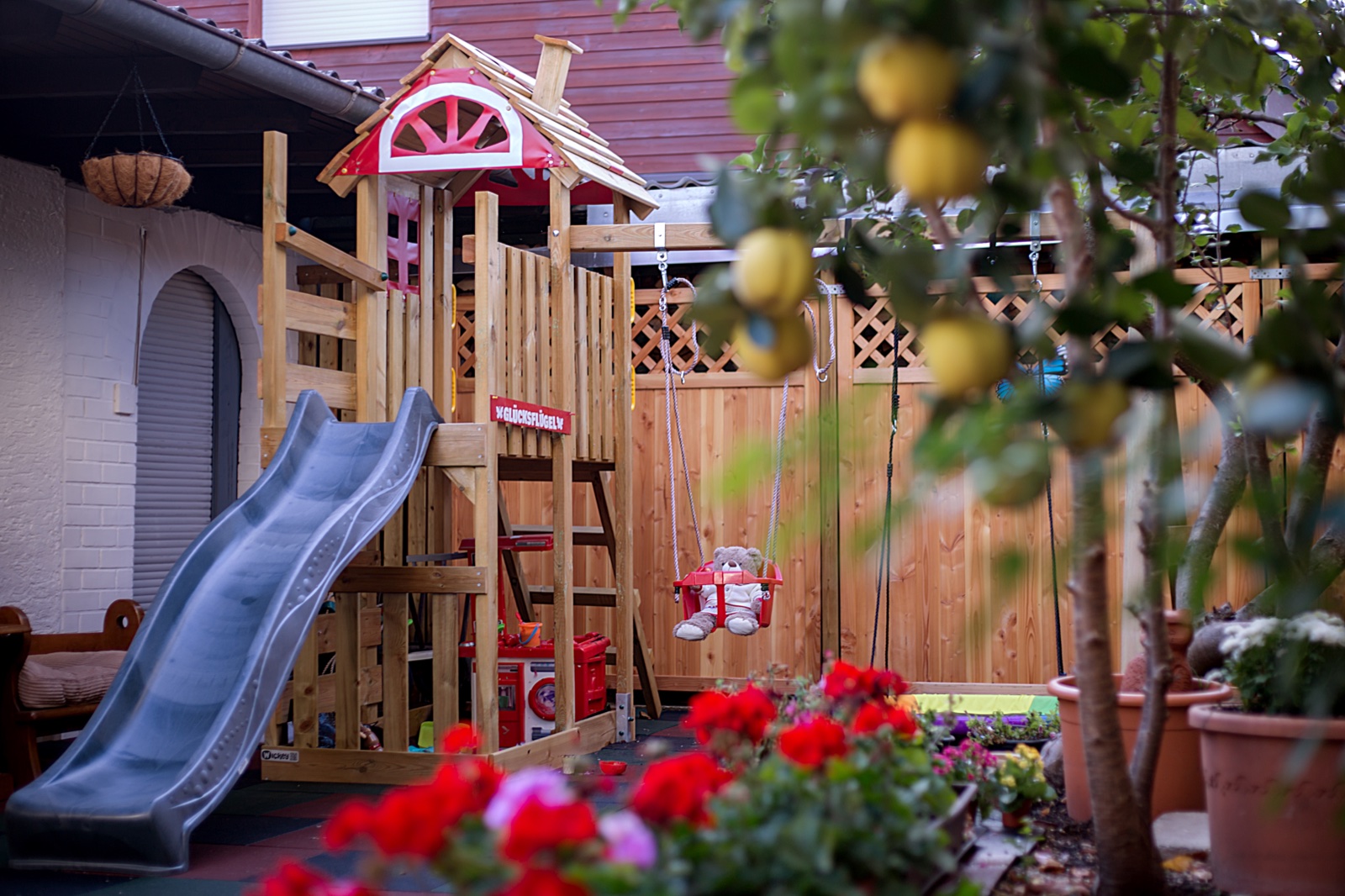 Garten mit hölzernem Spielturm, Rutsche, Schaukel und Blumen