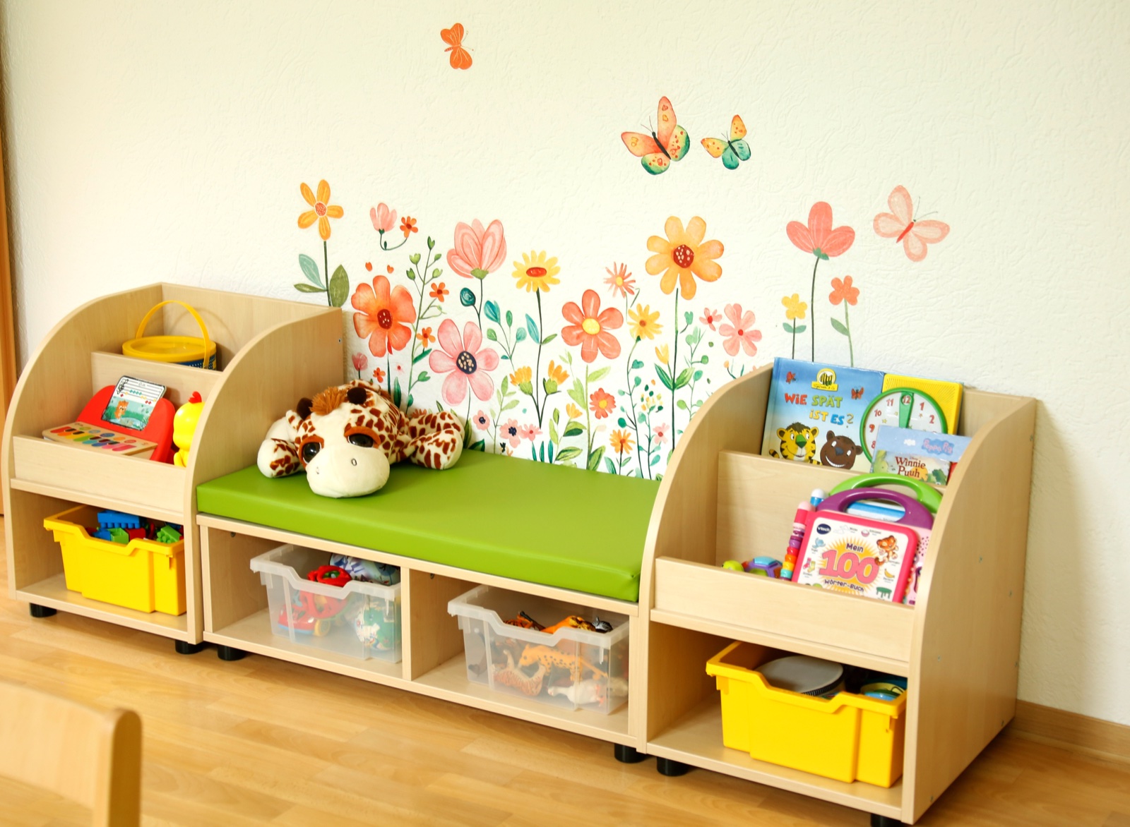 Lernbereich mit Bücherregalen, grüner Sitzbank und bunten Blumen an der Wand